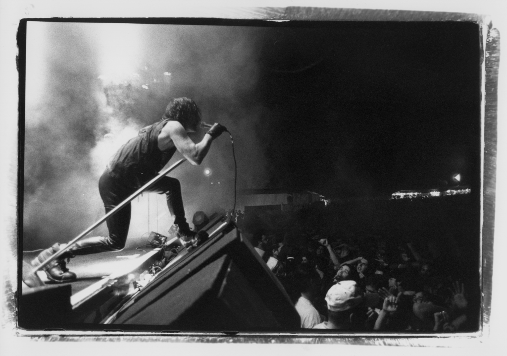 a black and white photo of a man standing with a microphone on the edge of a crowd