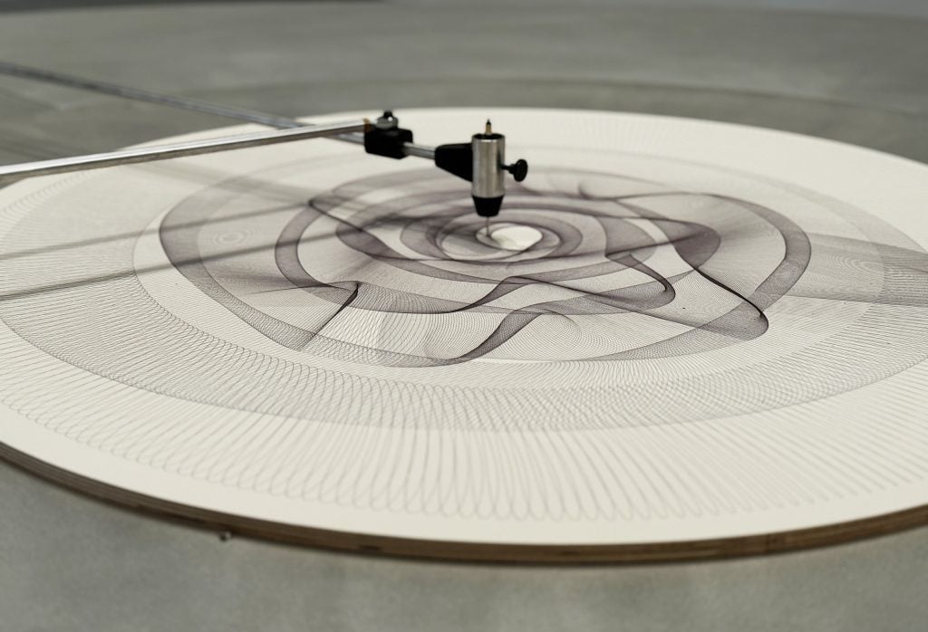 A stylus drawing an intricate radial pattern on a circular canvas