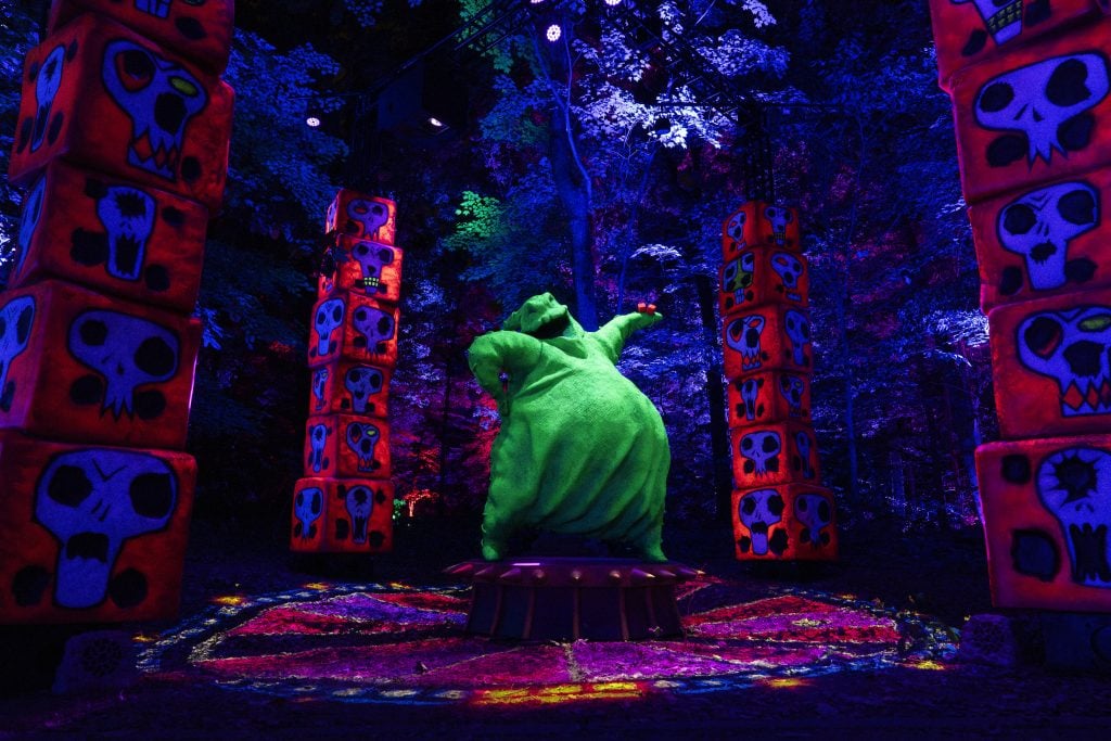 A photograph of a sculpture of the Oogie Boogie from the Nightmare Before Christmas surrounded by pillars of sculptural dice in a dark forest.