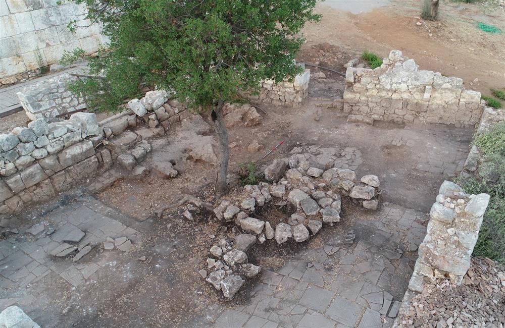 An aerial photograph of an archaeological dig site in Anataly, Türkiye, with a small rock formation in its center, marked by one green tree.