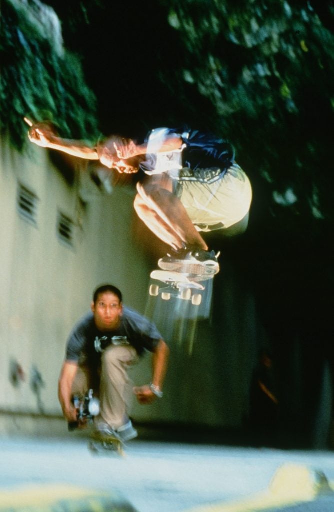 One young man on a skateboard flies through the air as another records him on video