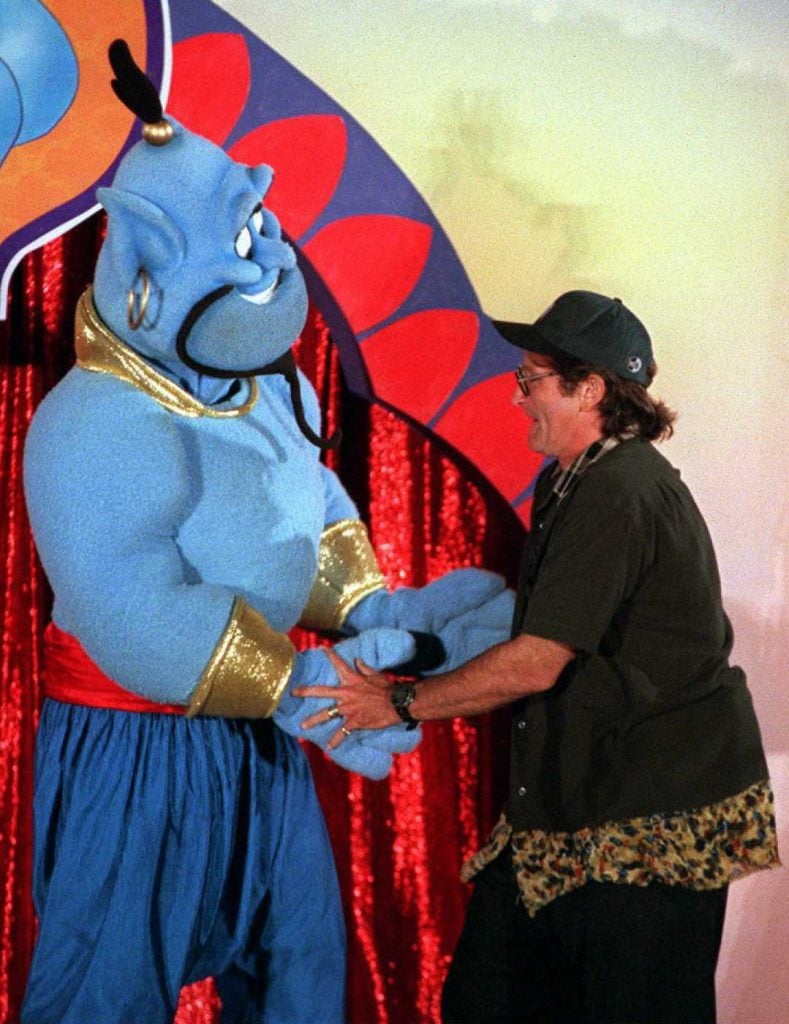 A photograph of Robin Williams dancing with an actor wearing a full costume of the genie from Aladdin.