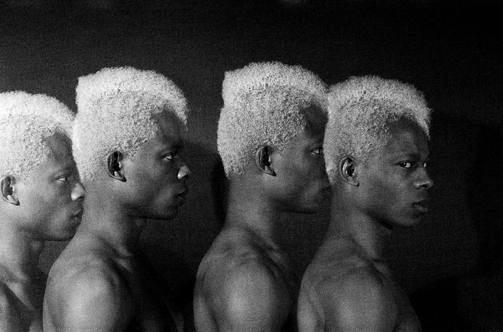 A black and white photo of four people who are the same standing front to back in side profile from the shoulders upto the camera. Included at the 2024 FotoFocus Biennial.