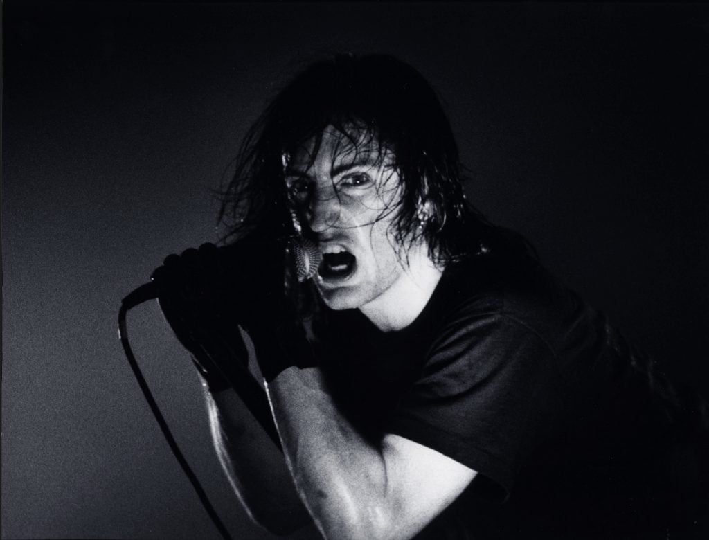 a man holds microphone in a black and white photograph he has an anguished facial expresion