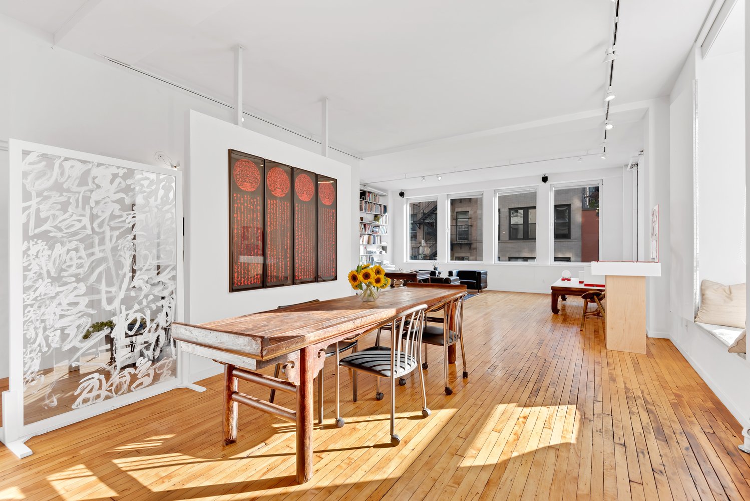 A photograph of a spacious, light-drenched, white-walled dining area surrounded by art.