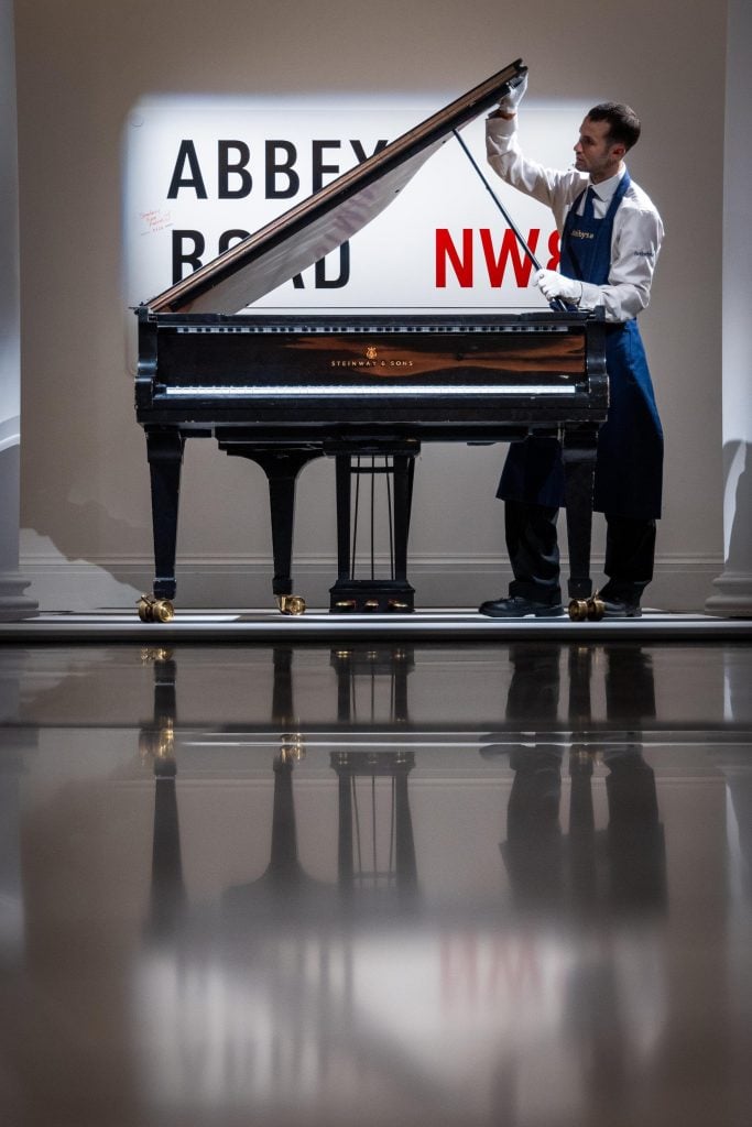 a piano with a man looking into it behind him the sign of Abbey Road is projected