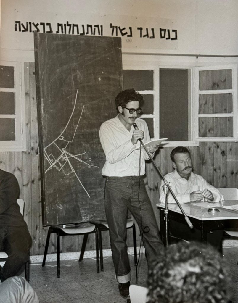 a black and white image of a man speaking into a microphone with a large map behind him