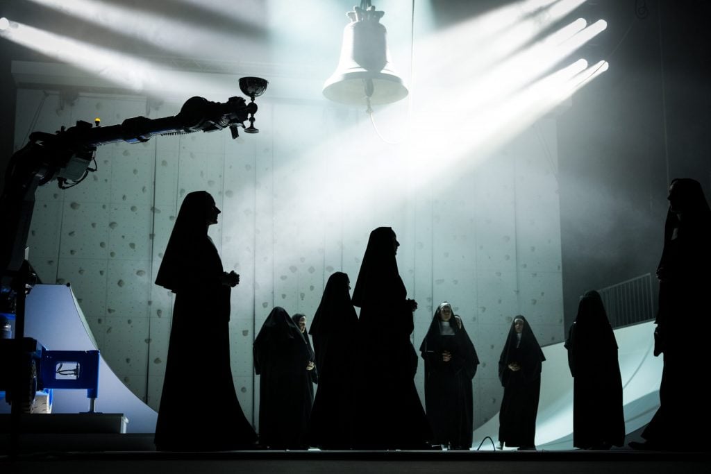 a scenen depcits nuns onstage at an opera with a robotic arm 