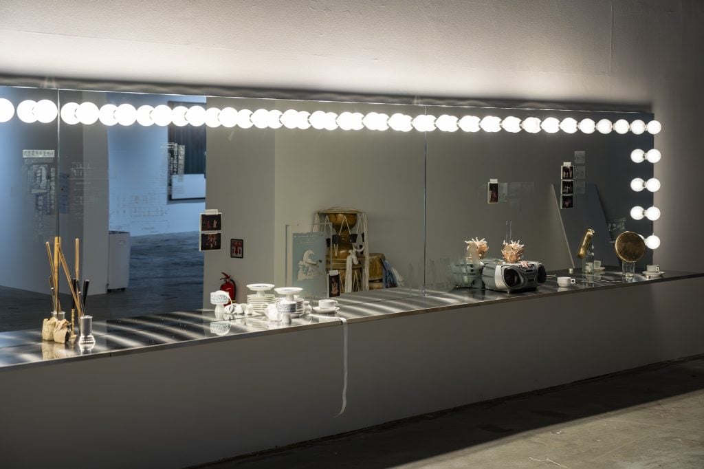 A long mirror with light bulbs on the edge on top and on the side, objects on the bench in front of the large mirror