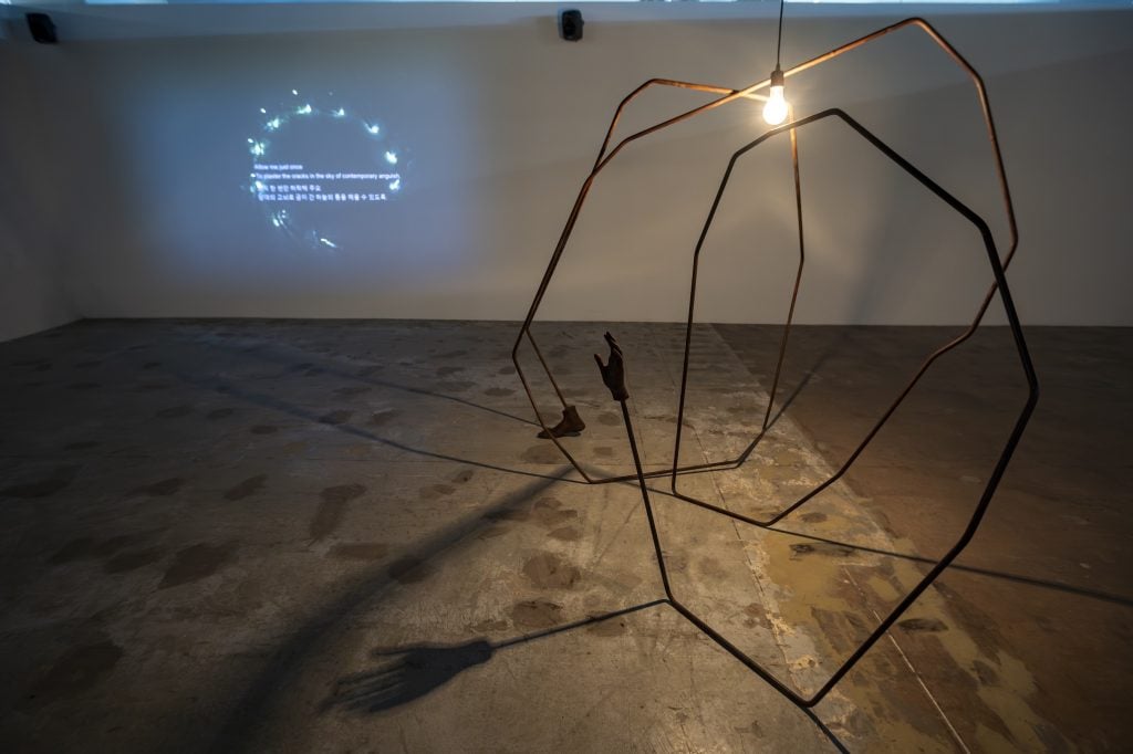 A sculpture looks like a spider on the right, on the left, an image of light in circle is projected onto the wall 