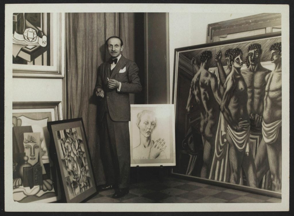 old man standing in front of a collection of paintings