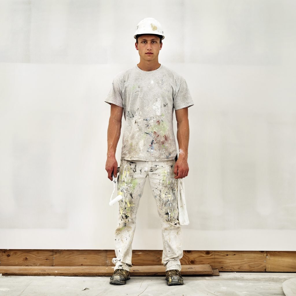 a construction worker painter in a splattered white shirt and paints and construction hat holding his roller