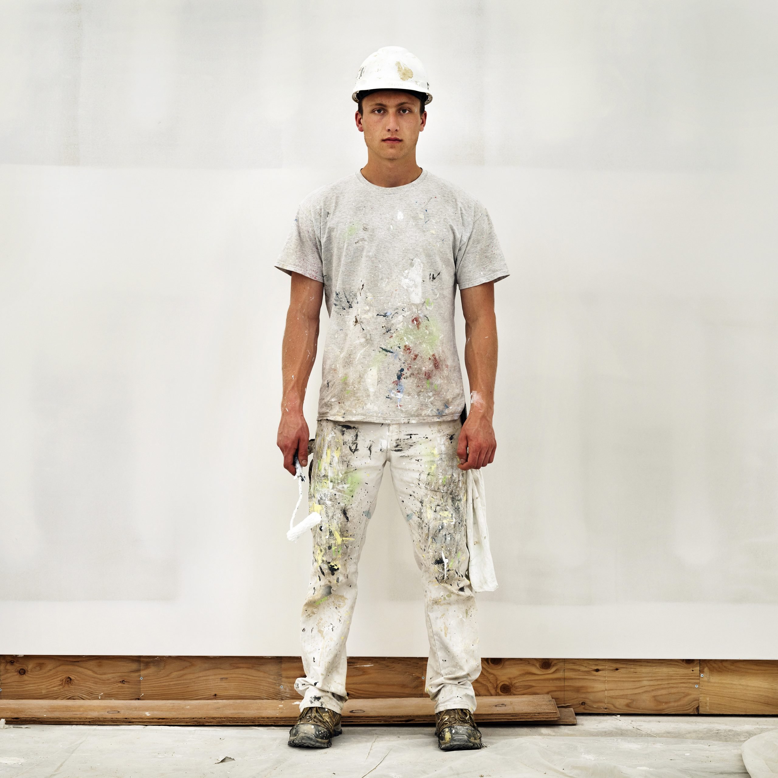 a construction worker painter in a splattered white shirt and paints and construction hat holding his roller