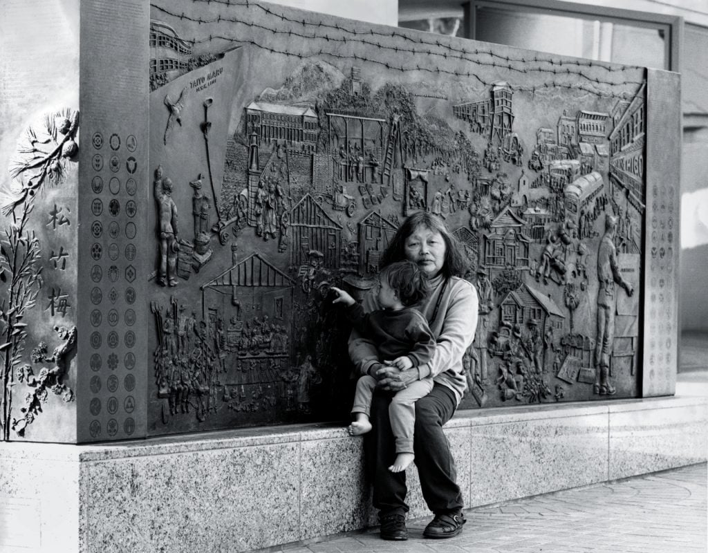 A black and photo of Ruth Asawa and her granddaughter Emma Lanier with Japanese American Internment Memorial (1990–94), commissioned by the City of San José; 300 South First Street, San José.