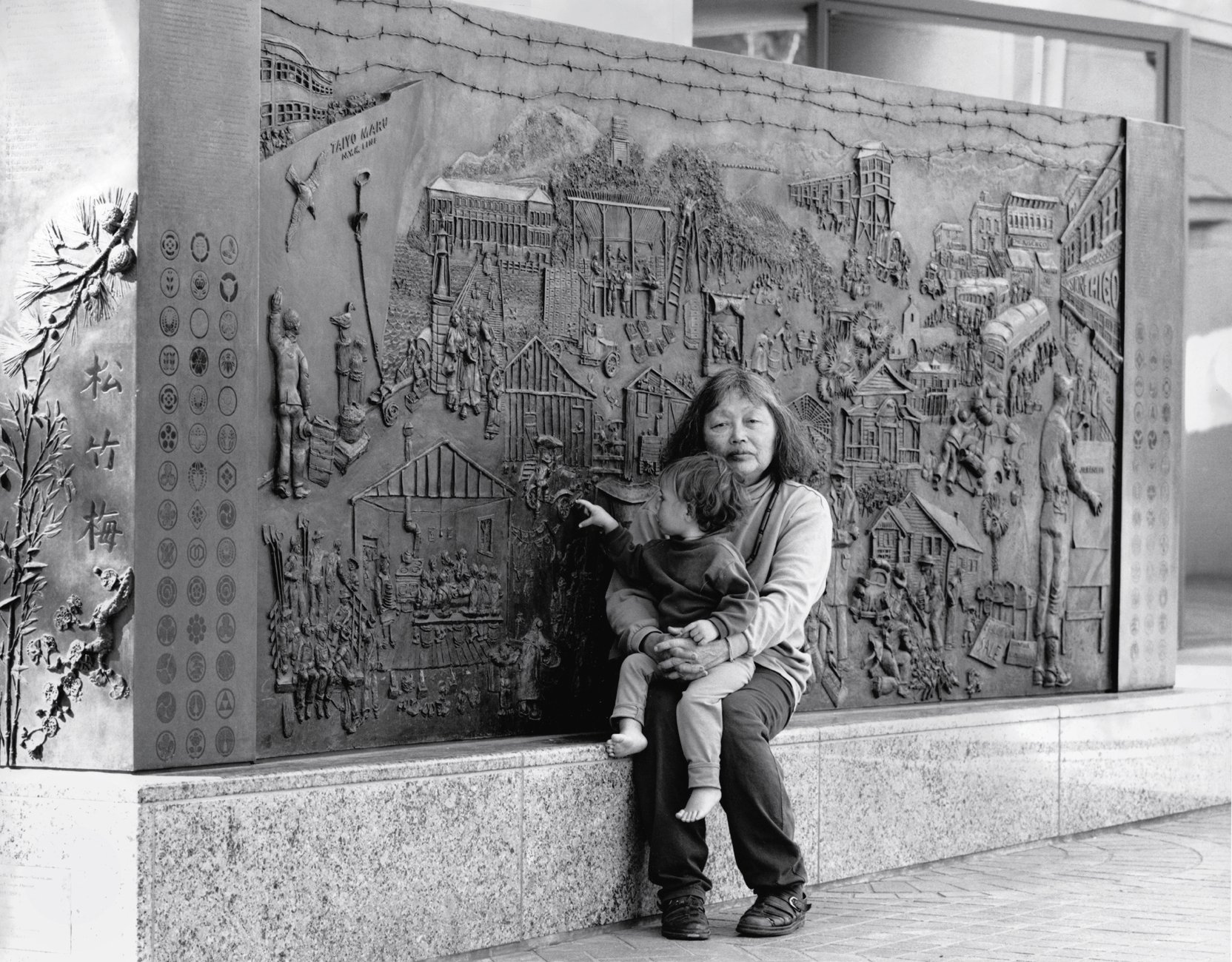 A black and photo of Ruth Asawa and her granddaughter Emma Lanier with Japanese American Internment Memorial (1990–94), commissioned by the City of San José; 300 South First Street, San José.