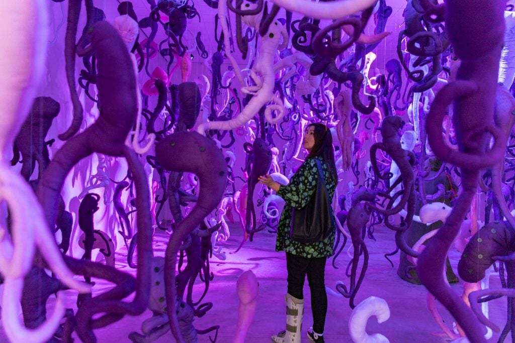 a woman wearing a boot brace is surrounded by a hanging sculpture installation, bathed in purple light