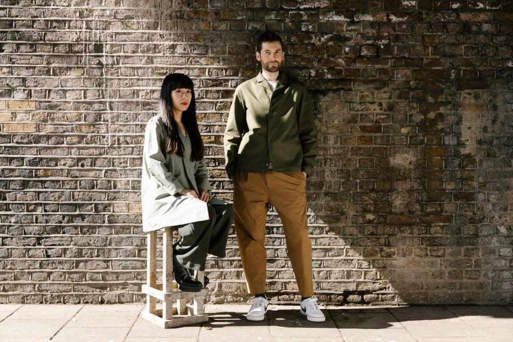 a man and woman stand in front of a brick wall