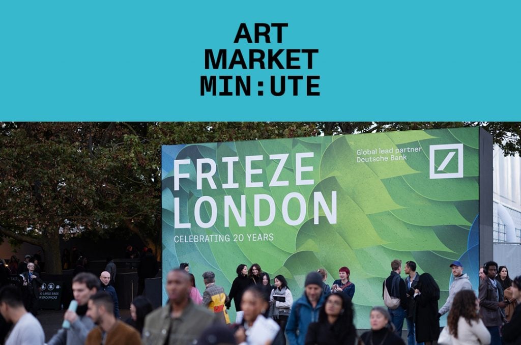 a crowd of people walk by a large outdoor sign that reads frieze london