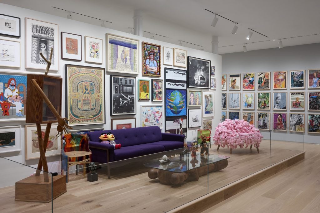 A variety of artworks hang on a white wall. A couch sits beneath them.