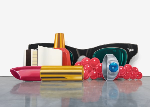 This image depicts a composition of oversized, colorful objects on a reflective surface, featuring a stylized pair of black sunglasses with green lenses in the background. In front of the sunglasses are various objects: a tube of lipstick with a metallic gold and pink body, a cluster of bright red beads, a silver ring with a blue gemstone, a bottle of nail polish, and what appears to be an open book or notepad. The objects are arranged in a playful, surreal manner, blending elements of fashion, accessories, and everyday items. The overall aesthetic evokes a sense of Pop Art style.