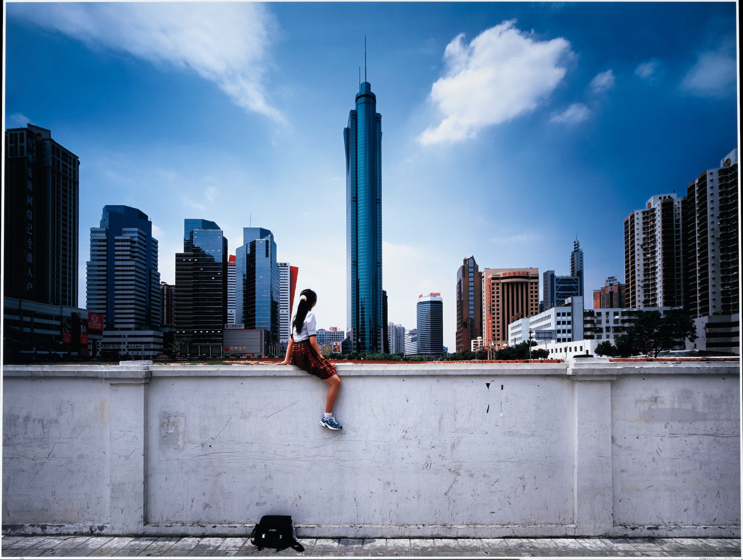 a photo of a girl sitting on a white wall with talk buildings behind her