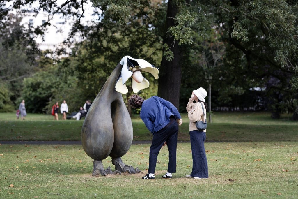 two people look intently at a sculpture of a flower in a park