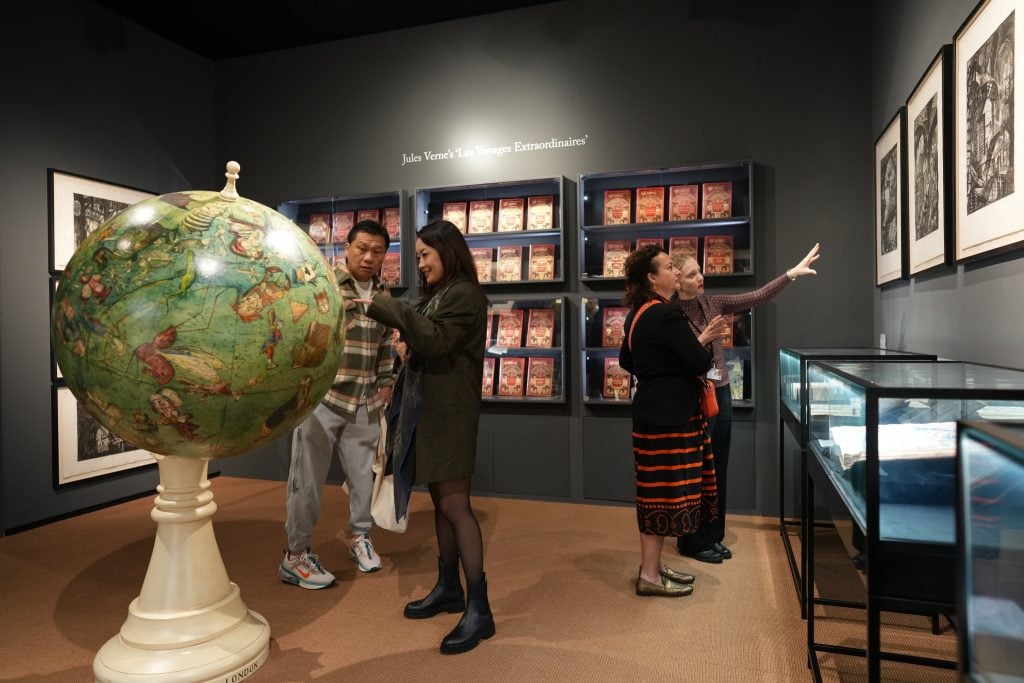 Crowd looking at artworks on display. An East Asian couple on the left studies a model of a globe