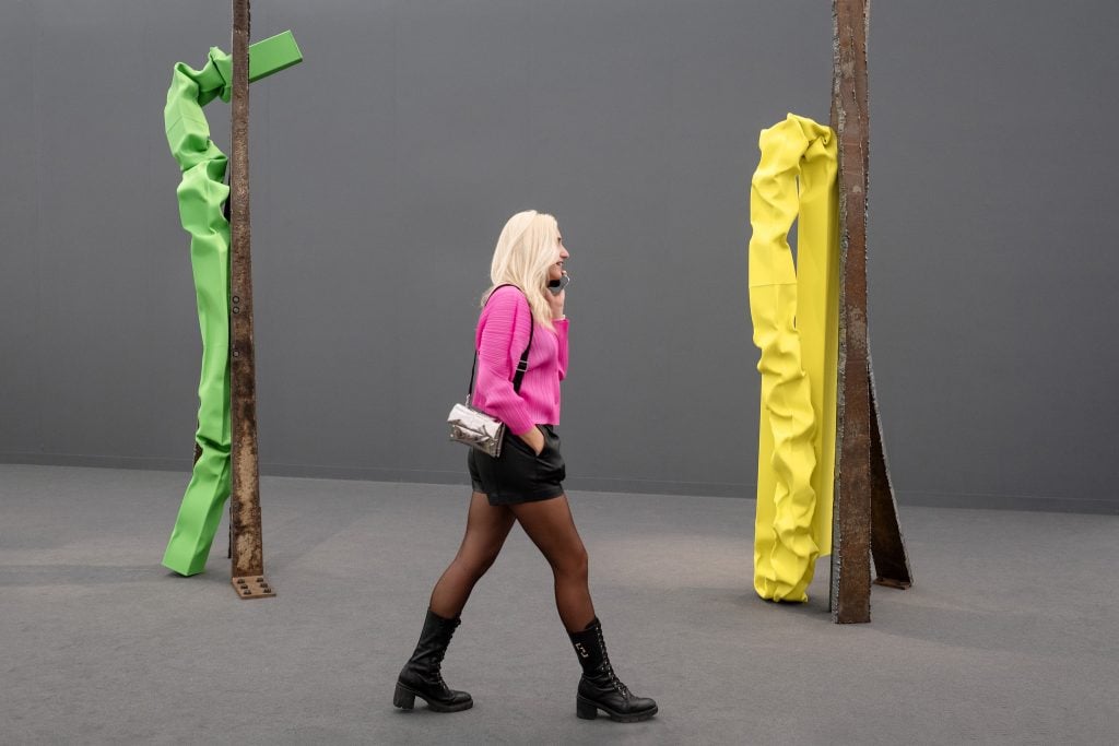 Woman in a pink sweater walking past colorful sculptures at Frieze art fair.