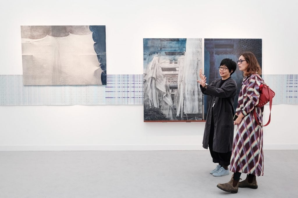 Two people discussing abstract paintings displayed at Frieze art fair