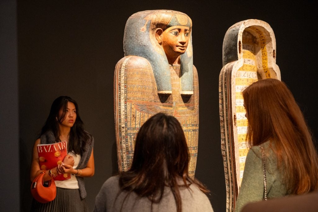 Visitors viewing Egyptian sarcophagi at an art fair exhibit.