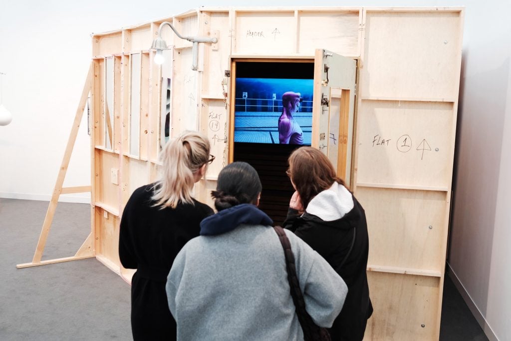 Attendees observing a video installation through a wooden structure at Frieze art fair.