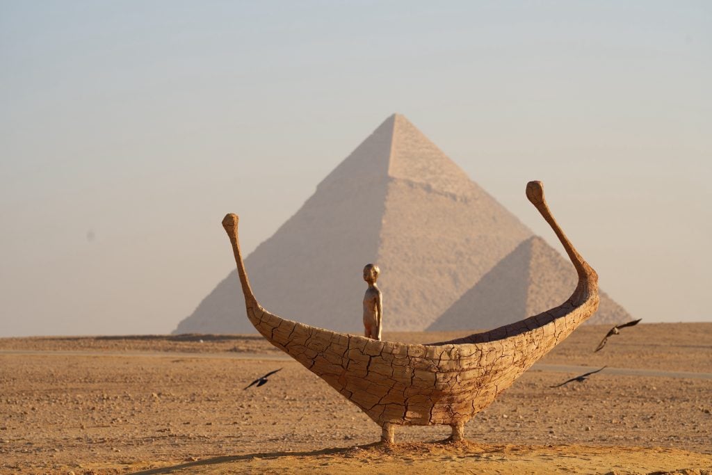 a small sculpture of a man in a boat stands before the pyramids of giza