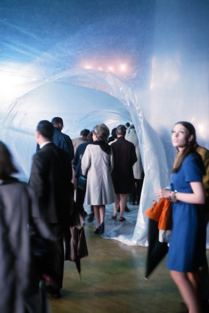 A crowd of people walking through a tunnel of plastic sheets