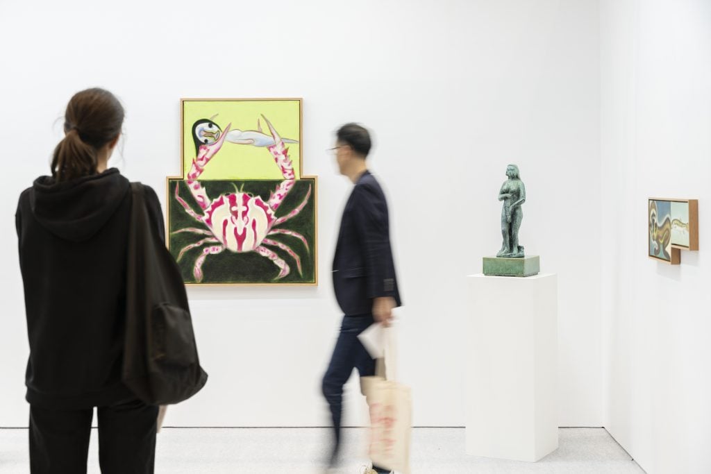 People looking at an artwork, which features a painting of a crab, on a white wall