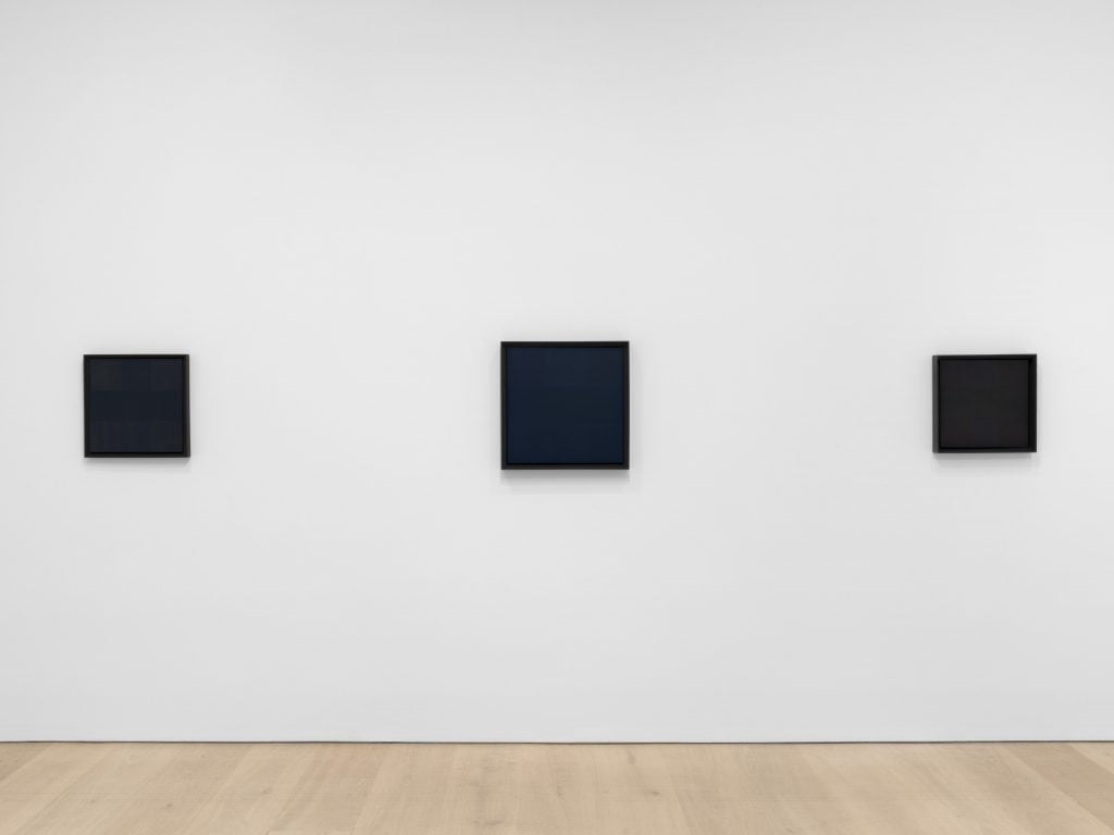 three monochrome paintings in black hang on the wall in a gallery 