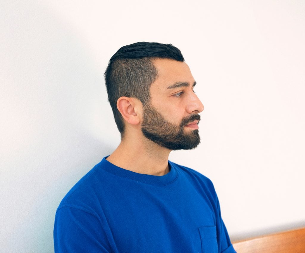 a photograph of a young man in profile who is wearing a blue t-shirt against a white background