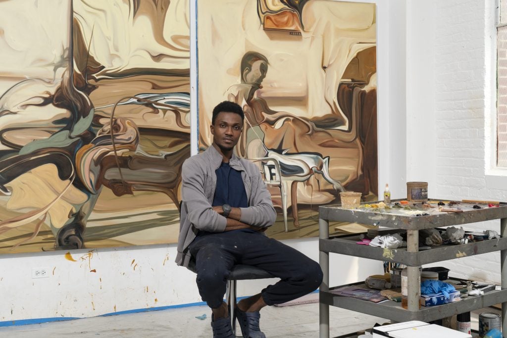 a photographic portrait of a young black man in a studio with paintings behind him