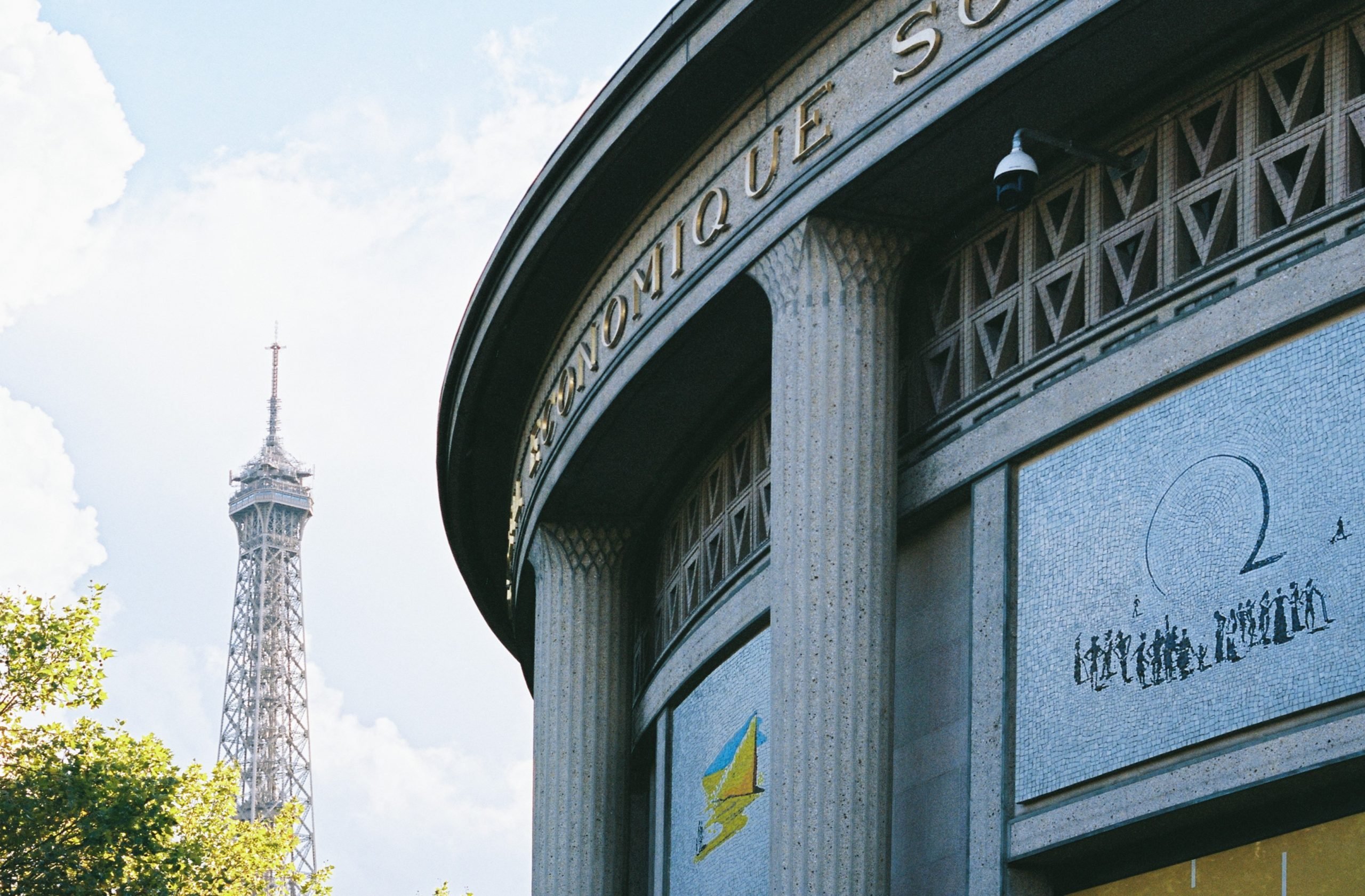 Eiffel Tower seen behind the corner of a curved building with mosaic details.