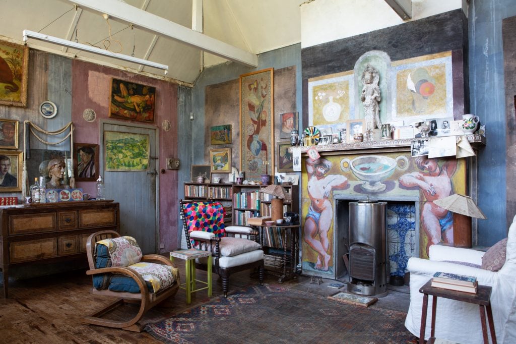 an interior that is very colorful and arty, the walls are covered in little paintings, there are lots of books and a fireplace with some 20th century furniture