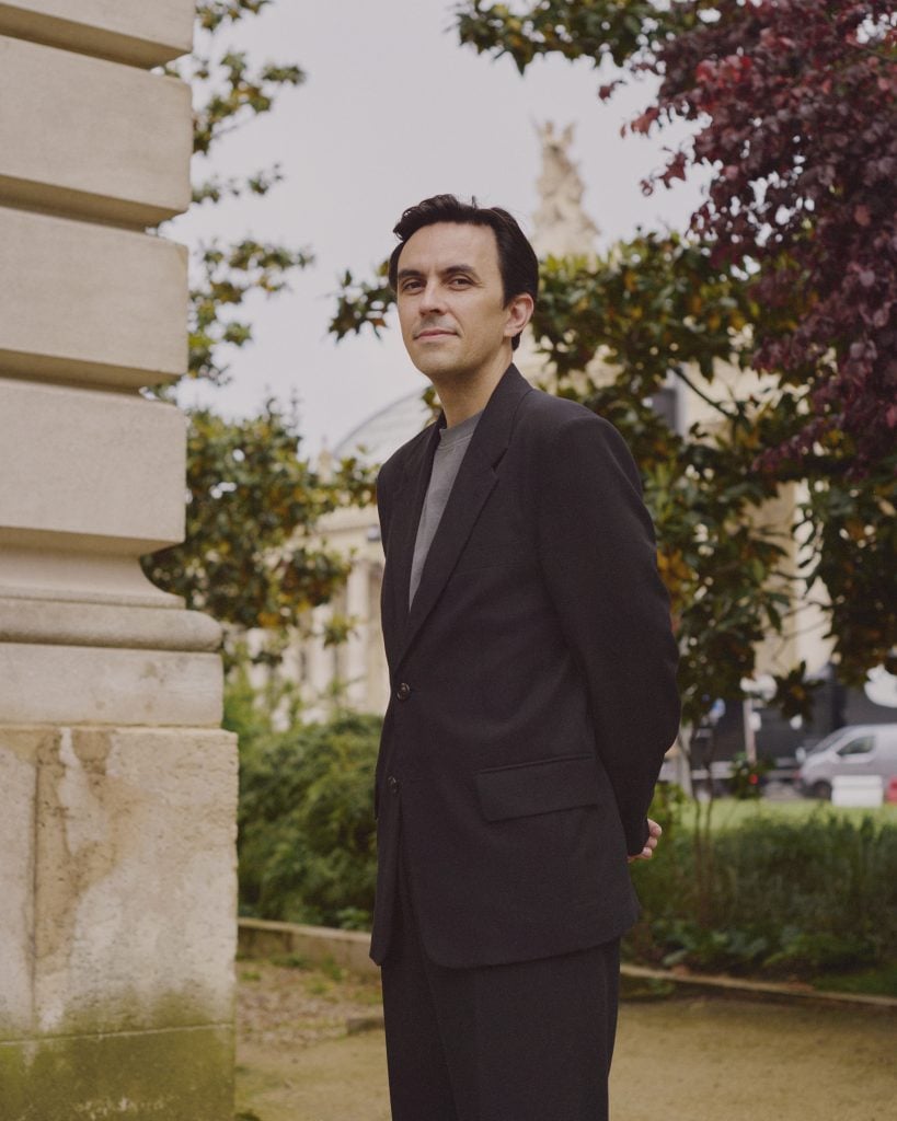 a well-dressed white man stands in a garden