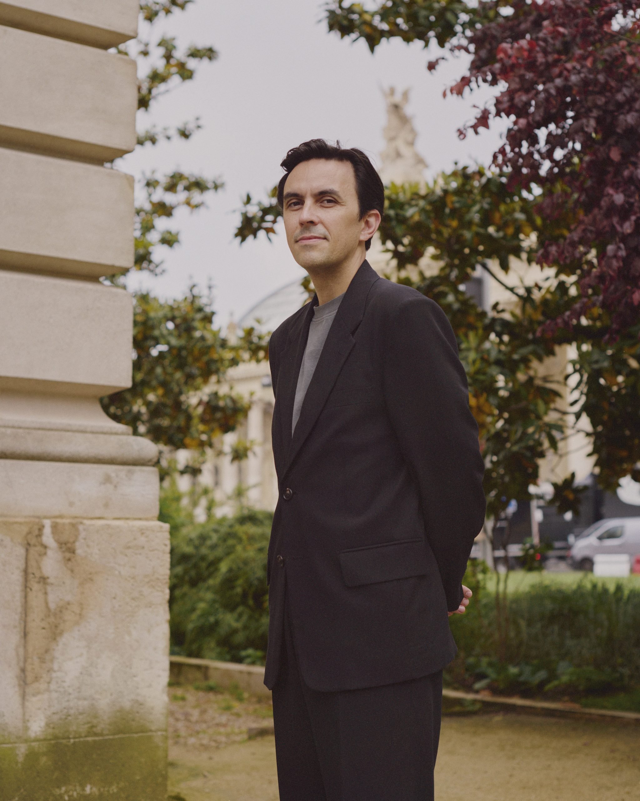 a well-dressed white man stands in a garden