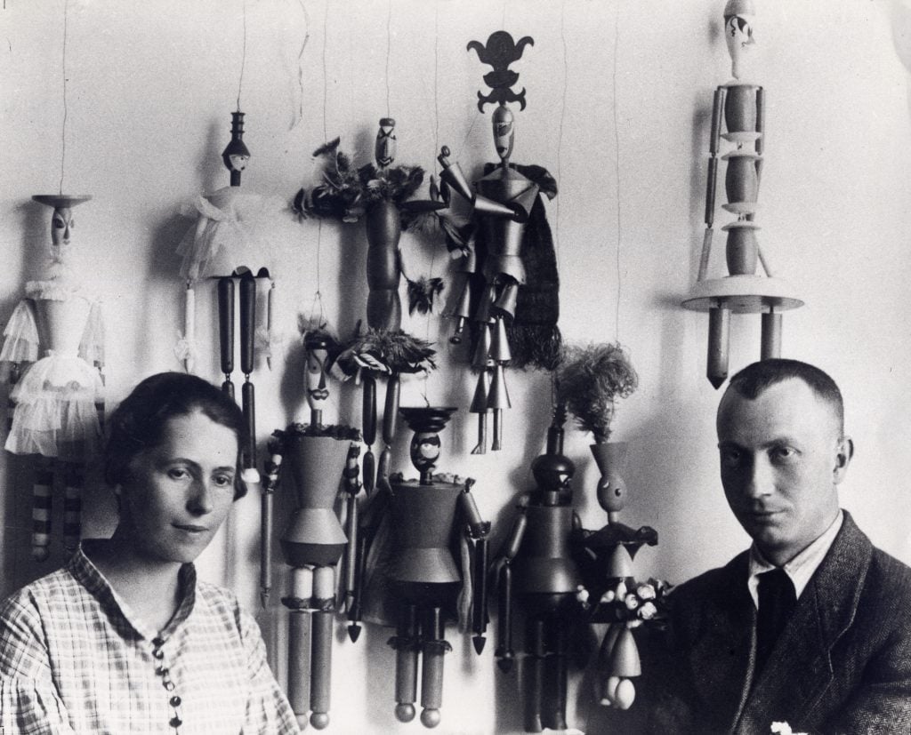 a man and a woman surrounded by puppet sculptures