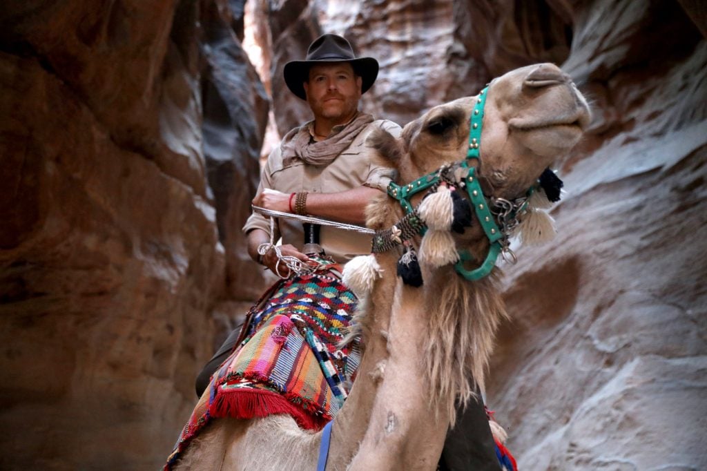 a man in a fedora rides a camel at Petra