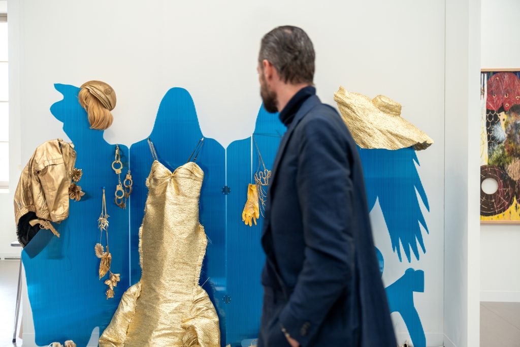 Man observes golden garments displayed on a blue backdrop at an art exhibition.