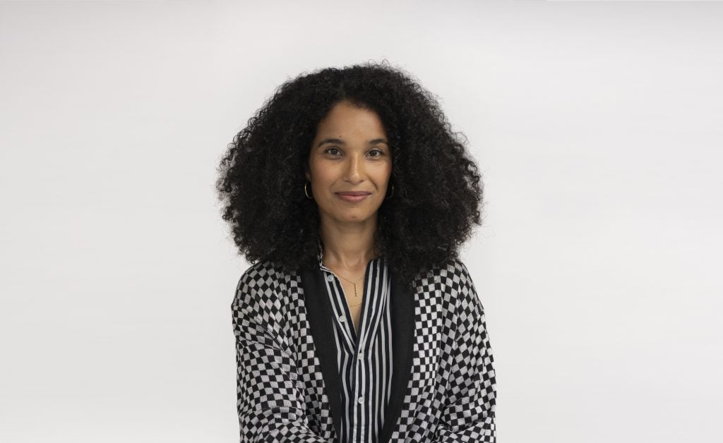 a photo of a woman with dark curly hair in a black and white patterned shirt