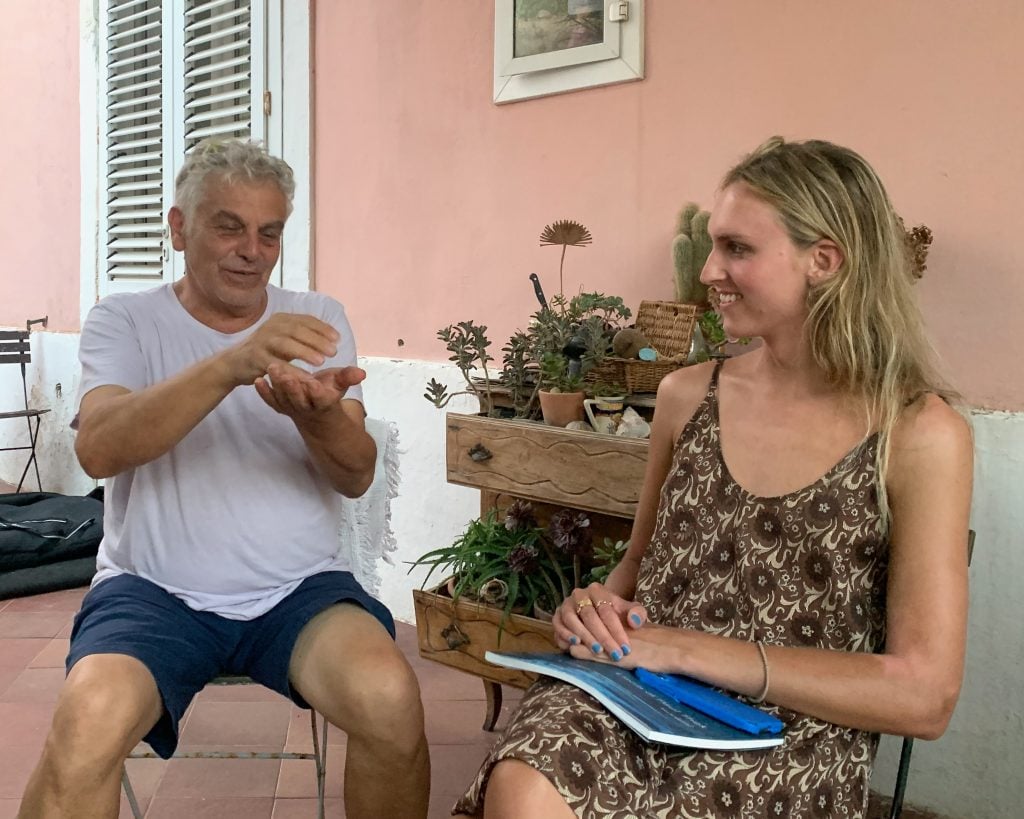 a man and woman sit outside of a pink walled Mediterranean abode 