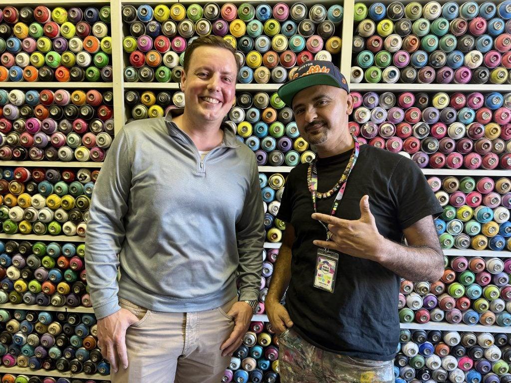 Garrett Clayton and Mario Enrique Figueroa Jr., or GONZO247, at Luckie's Pocket, a nonprofit art center they are opening at a historic Houston schoolhouse. They are standing in front of shelves filled with spray paint cans. 