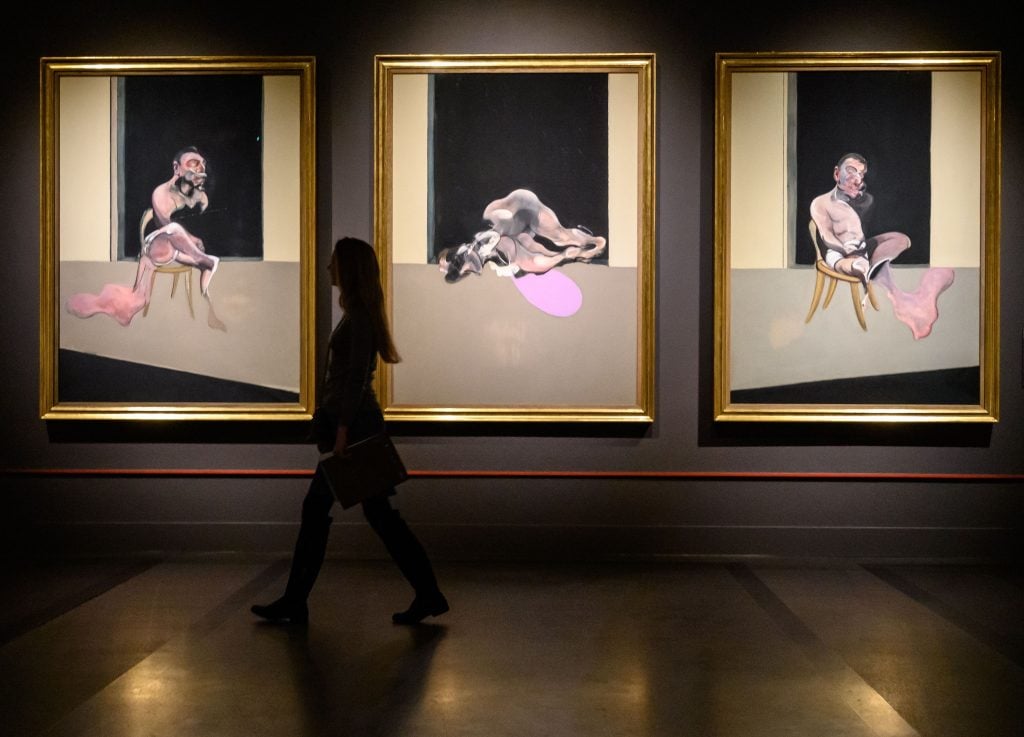 a woman walks past a Triptych in a gallery