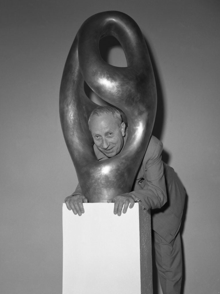 French sculptor and painter Hans Jean Arp, wearing a suit, with glasses in his pocket, passing his head through one of his bronze sculptures