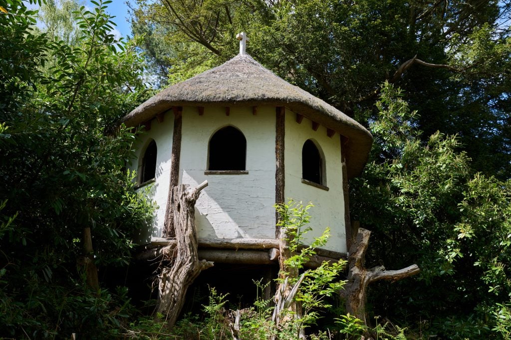 a rustic white structure in the woods with brown roof and windows, a depiction of Hermits in art